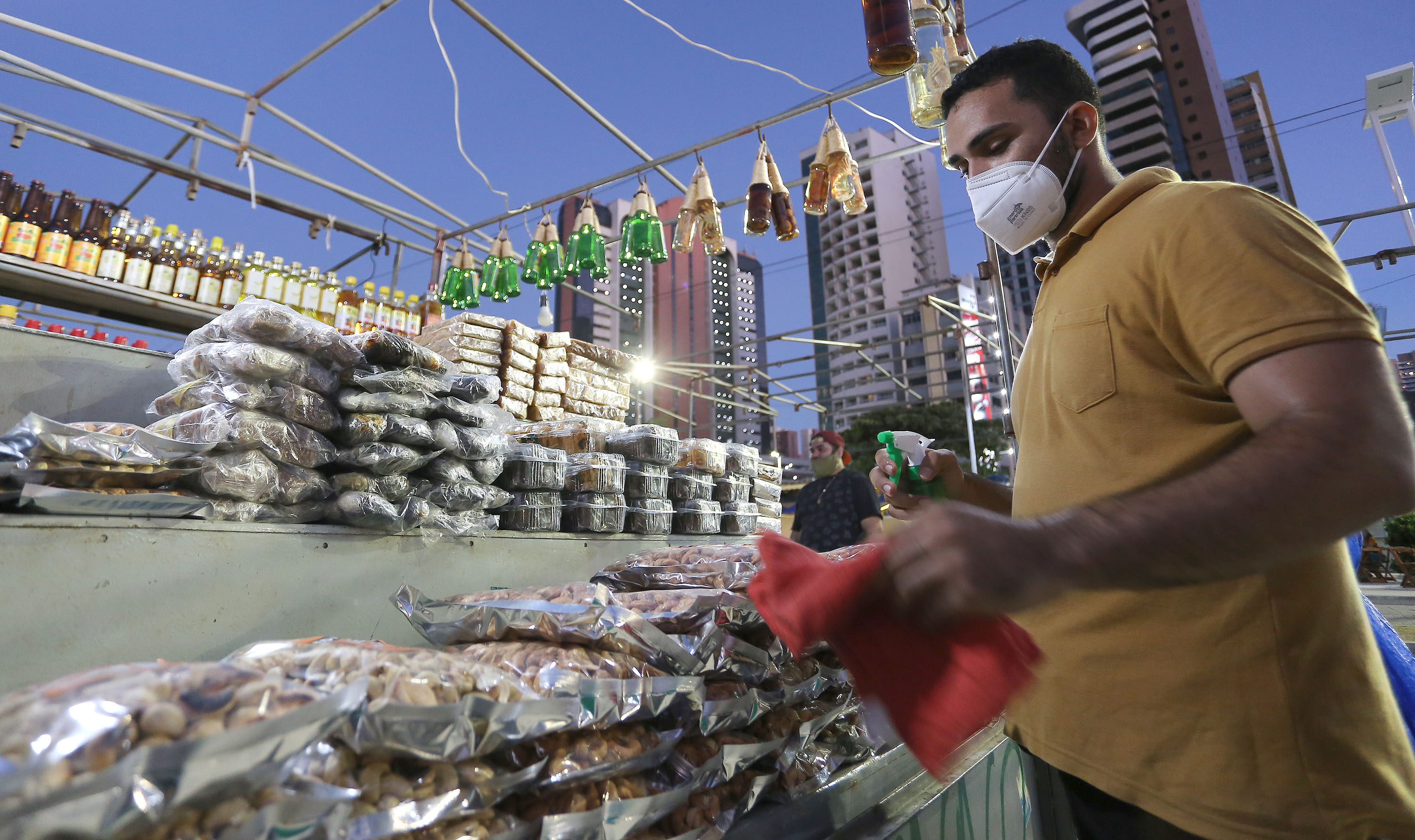 homem na frente de uma barraca de que vende molhos, mel e outros produtos de alimentação na feira da beira-mar